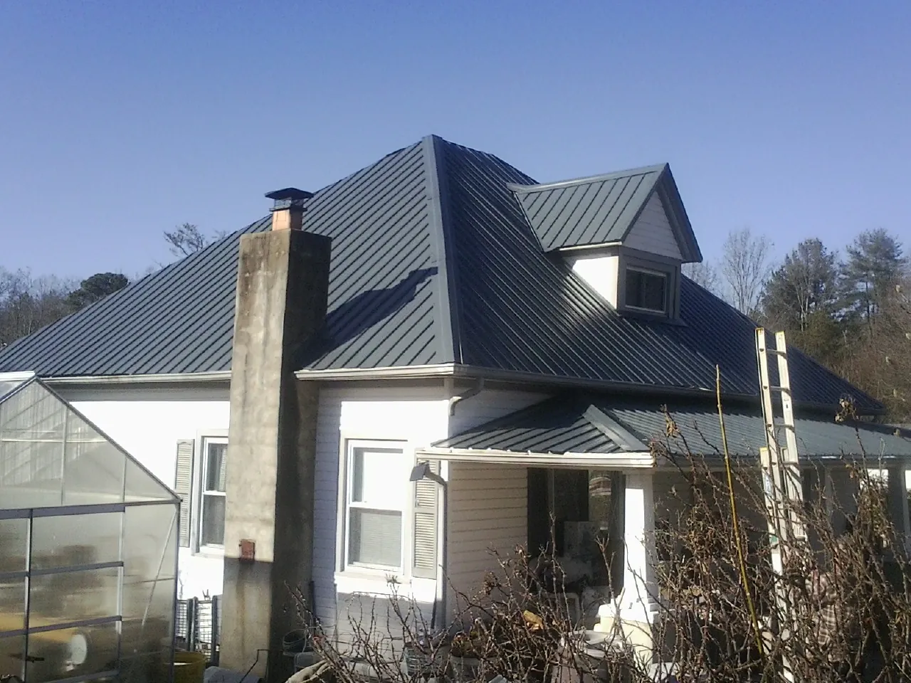 Dark blue standing seam metal roof on a white farmhouse with dormer — Slate & Tile Roof Repair by Roofing Brothers in Beaman