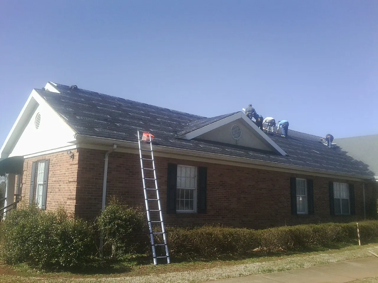 Crew tearing shingles off a brick ranch roof with a ladder set — Emergency Roof Repair work by our crew in Beaman