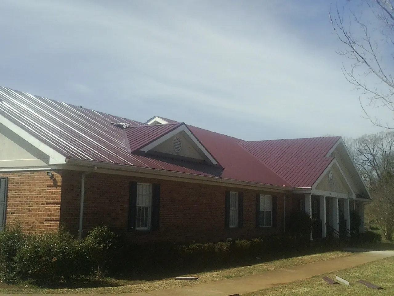 Red metal roof with gabled entries on a long brick building, from a Hail Damage Roof Repair job in Beaman
