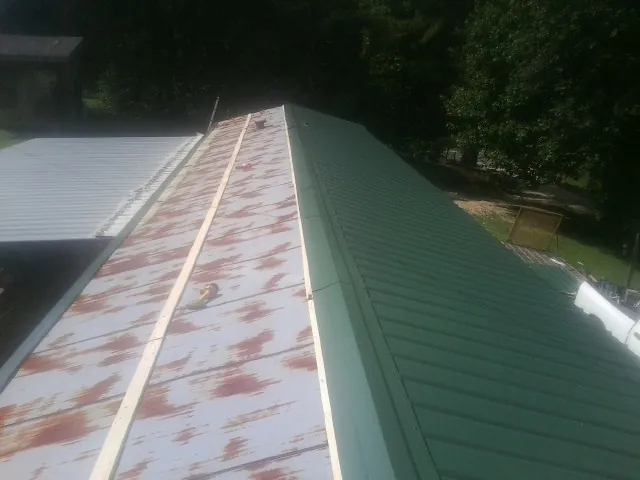 Old rusted panels beside newly installed green metal roofing — Wind Damage Roof Repair by Roofing Brothers in Beaman