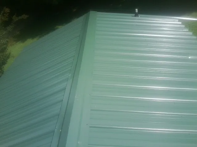 New green metal panels meeting at the ridge of a roof — Flat Roof Repair work by our crew in Beaman