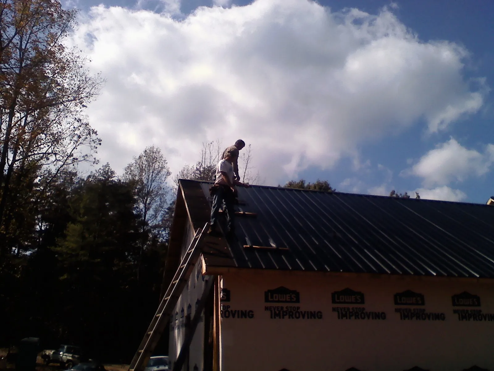 Roofer fastening dark metal panels high against a cloudy sky, from a Roof Inspection job in Beaman