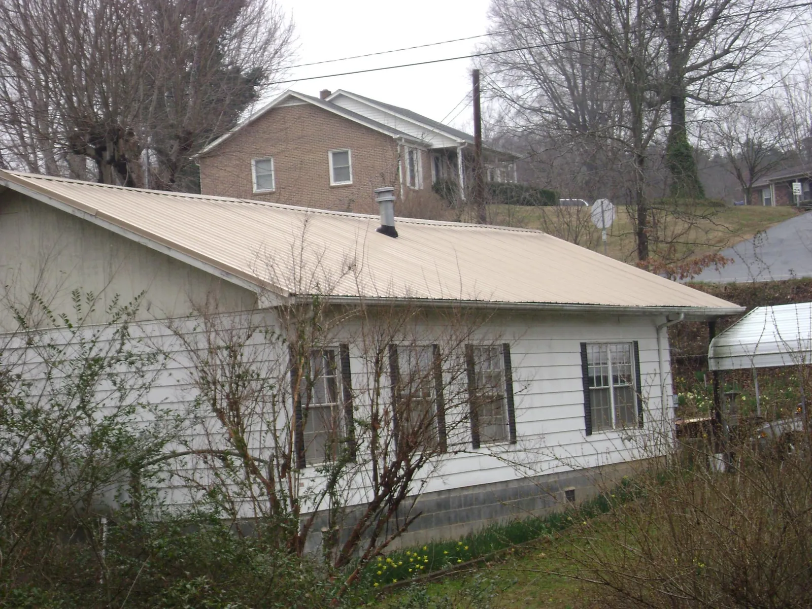 Tan metal roof on a white sided house set into a hillside — Commercial Roofing by Roofing Brothers in Beaman