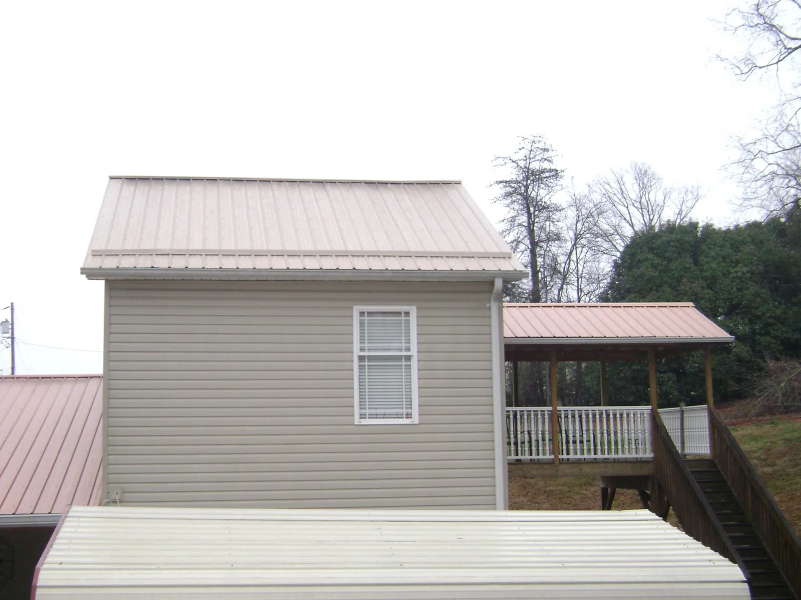 Tan metal roofs on a two story addition and attached porch, from a Roof Replacement job in Beaman